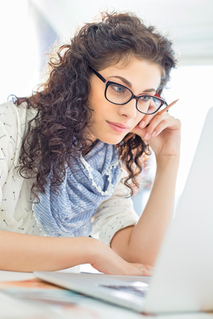 Businesswoman using laptop at desk in creative officeの写真素材