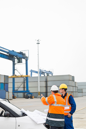 Workers discussing over blueprint in shipping yardの写真素材