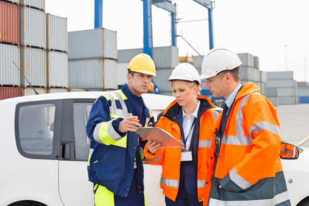 Workers discussing over clipboard beside car in shipping yardの写真素材