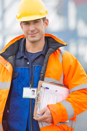 Portrait of confident mid adult man with clipboard in shipping yardの写真素材
