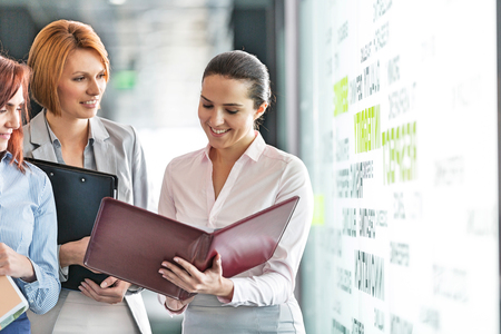 Businesswomen with file folders discussing in office corridorの写真素材