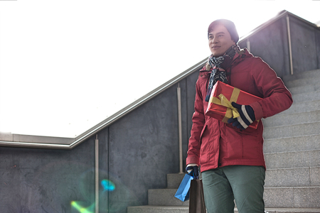 Smiling man holding gifts while moving down stepsの写真素材