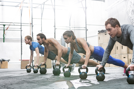 Dedicated people doing pushups with kettlebells at crossfit gymの写真素材