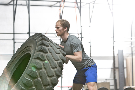 Side view of dedicated man flipping tire in crossfit gymの写真素材