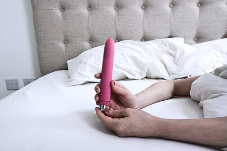 Woman inserting batteries into a Pink Vibrator Dildo in Bedの写真素材