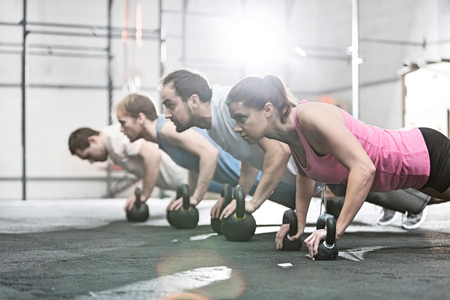 Side view of determined people doing pushups with kettlebells at crossfit gymの写真素材