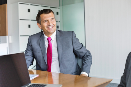Happy mature businessman sitting at desk in officeの写真素材
