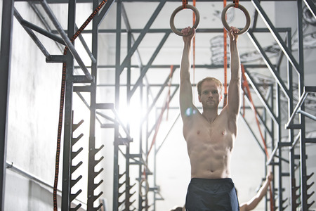 Confident man exercising with gymnastic rings in crossfit gymの写真素材