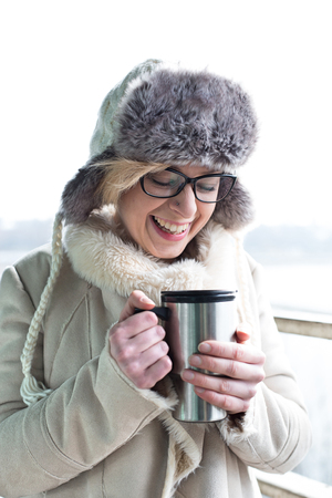 Cheerful woman in warm clothing holding insulated drink containerの写真素材
