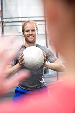 Happy man throwing medicine ball towards woman in crossfit gymの写真素材