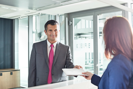 Businessman receiving document from receptionist in officeの写真素材