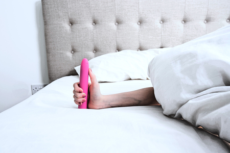 Woman holding a Pink Vibrator Dildo in Bedの写真素材