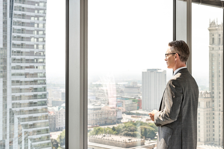 Side view of mature businessman looking through office windowの写真素材