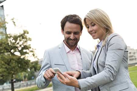 Happy business couple using smart phone at parkの写真素材