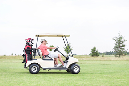 Side view of couple sitting in golf cart against clear skyの写真素材