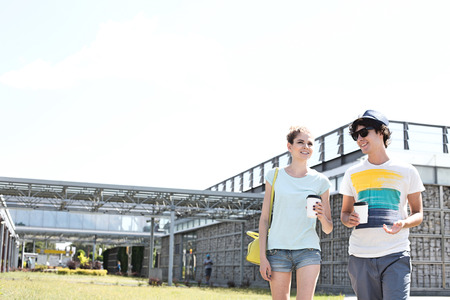 Smiling couple holding disposable cups while walking at parkの写真素材