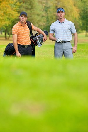 Young men standing on golf course carrying bagsの写真素材