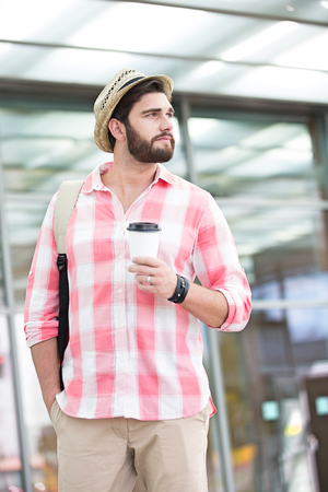 Thoughtful man looking away while holding disposable cup in cityの写真素材