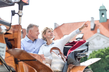 Middle-aged woman showing something to man while sitting in horse cartの写真素材