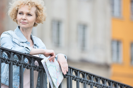 Thoughtful middle-aged woman holding map while leaning on railingの写真素材