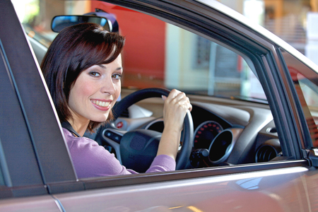 Portrait of young woman sitting in driver's seat at car dealershipの写真素材