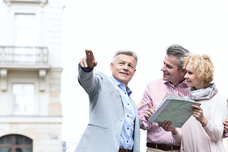Man showing direction to couple with road map in cityの写真素材