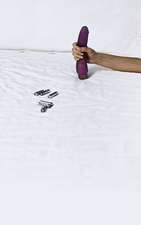 Woman's hand holding dildo in bedの写真素材