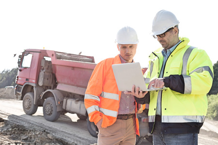 Engineers using laptop at construction site against clear sky on sunny day