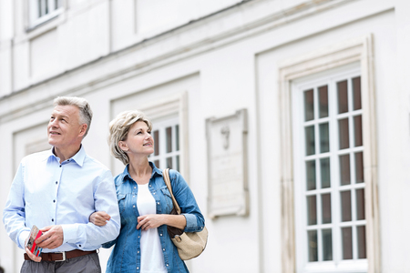 Smiling middle-aged couple standing with arm in arm outside buildingの写真素材