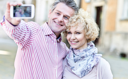 Happy middle-aged couple taking selfie through smart phone outdoorsの写真素材