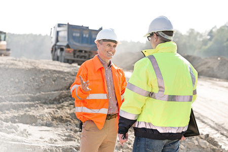 Happy engineer talking to colleague at construction site on sunny dayの写真素材