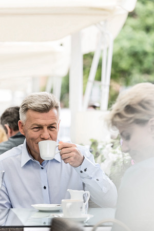 Middle-aged man looking at woman while having coffee at sidewalk cafeの写真素材
