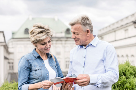 Middle-aged couple reading guidebook outside buildingの写真素材