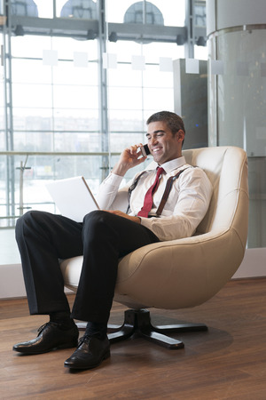 Businessman in arm chair working on laptop on the phoneの写真素材