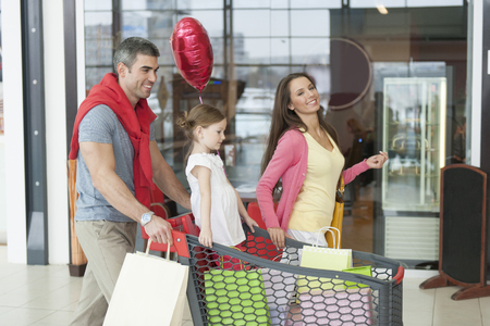 Father and mother push young daughter in shopping trolley through mallの写真素材