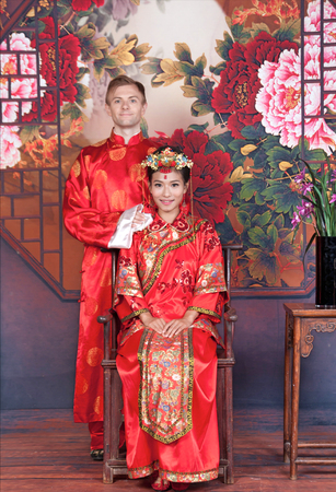 Mixed Race Bride and Groom in Studio wearing traditional Chinese wedding outfitsの写真素材