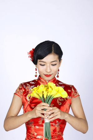 pretty chinese young woman holding a bunch of yellow daffodilsの写真素材