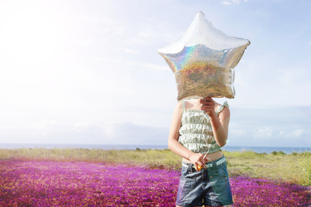 Front view of preadolescent girl holding star shaped balloon in front of her face while standing at flower fieldの写真素材