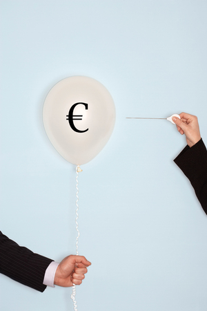 Cropped hands holding needle and popping balloon with EURO symbolの写真素材