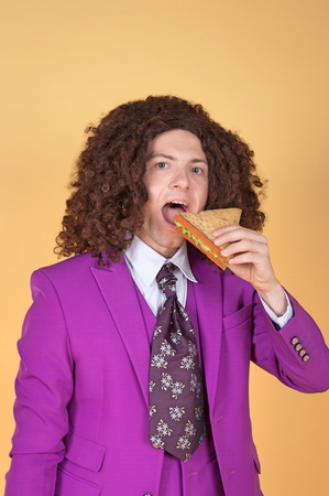 Caucasian man with afro wearing Purple Suit eating sandwichの写真素材