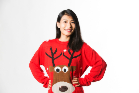 Portrait of woman in Christmas sweater standing with hands on hips over gray backgroundの写真素材