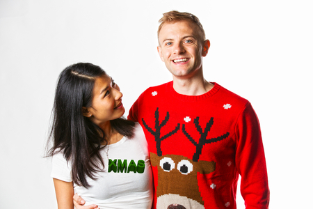 Portrait of happy multiethnic couple wearing christmas jumpers in studio whilst looking at each otherの写真素材