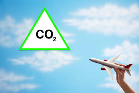 Closeup of woman's hand flying toy plane against cloudy sky with warning CO2 signの写真素材