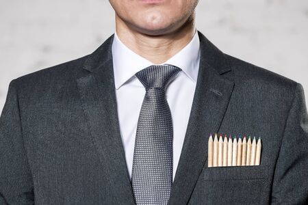 Midsection of businessman with colored pencils in pocket against wallの写真素材