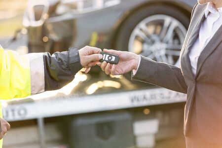 Cropped image of tow truck driver giving car key to businesswomanの写真素材