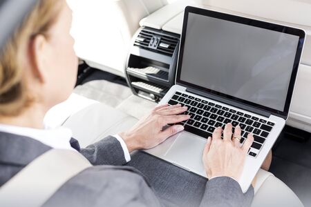 Mature businesswoman typing on laptop in carの写真素材
