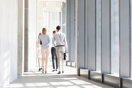 Rear view of business people walking in corridor at officeの写真素材
