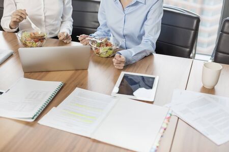 Midsection of businesswomen eating lunch while sitting at table in boardroomの写真素材