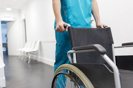 Midsection of nurse pushing wheelchair in hospital corridorの写真素材
