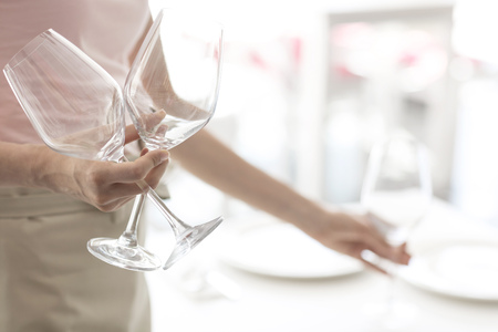 Midsection of young waitress holding wineglasses at restaurantの写真素材
